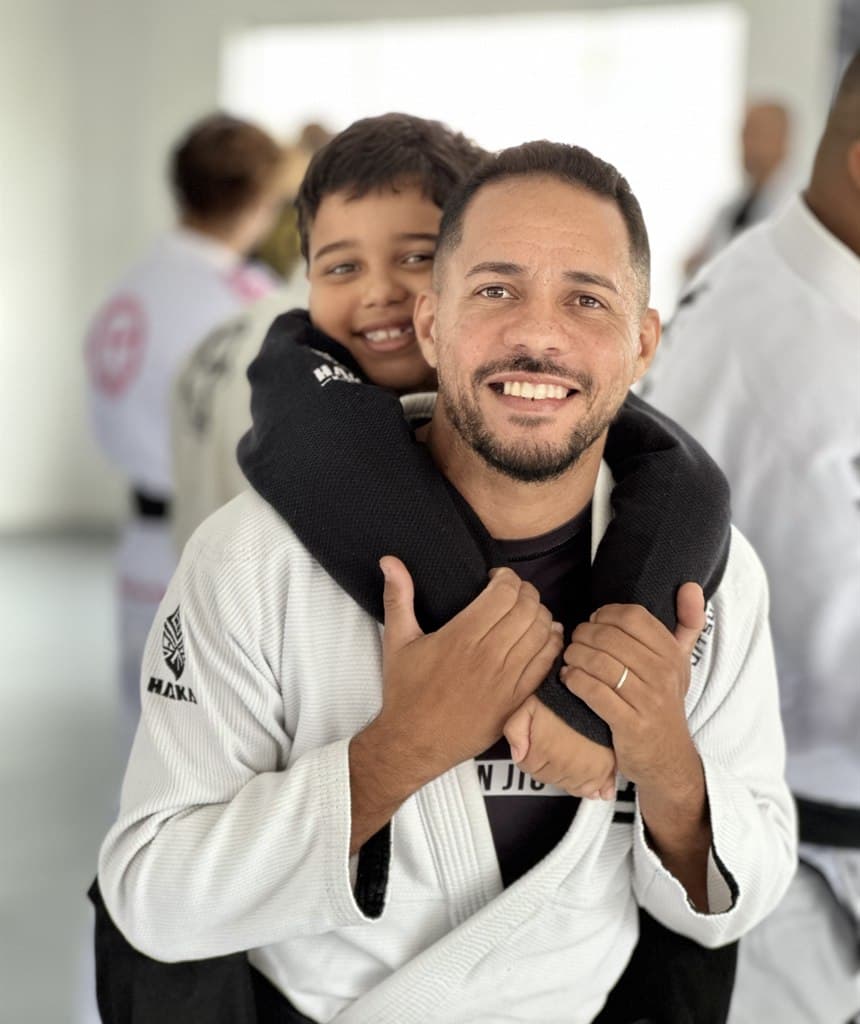 Professor da Team Cruz com uma criança sorridente no colo — Jiu-Jitsu Kids em Cajamar